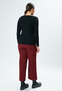 Top nero a maniche lunghe abbinato a pantaloni larghi bordeaux. Stivali platform neri completano l'outfit, caratterizzati da una texture liscia.