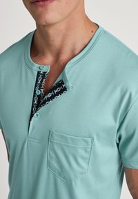 Lichtturquoise kortärmige shirt met een henley-kraag, voorzien van een contrasterende geblokte knoopsluiting en een borstzak. Glad textuur.