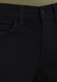 Jeans de mezclilla negra con una textura suave, que presentan un diseño clásico de cinco bolsillos, lazos para cinturón y un cierre de botón en la cintura.