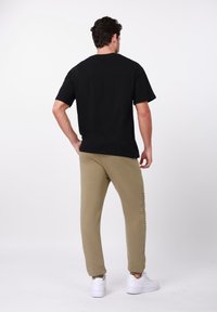 Μαύρο βαμβακερό T-shirt με κοντά μανίκια, συνδυασμένο με χακί φαρδιά παντελόνια jogger με λεπτομέρειες στο πλάι. Το σύνολο ολοκληρώνουν λευκά αθλητικά παπούτσια.