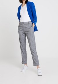 Niebieska marynarka na białej bluzce, zestawiona z szarymi spodniami w wzór i białymi trampkami. Kluczowe cechy to kraciasty wzór i dopasowany krój.