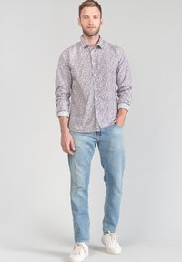 Camicia con bottoni con un leggero motivo floreale in tonalità di viola e bianco, abbinata a jeans blu chiaro e sneakers bianche.