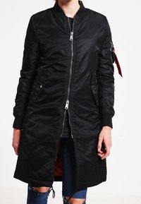 Czarna kurtka bombowca wykonana z gładkiego nylonu, z zapięciem na zamek, bocznymi kieszeniami i ściągaczami przy mankietach. Podszewka w pomarańczowym kolorze z detalem naszywki z boku.