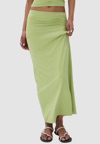 Lichtgroene maxi rok van zacht, rekbaar materiaal met geplooide details in de taille, gecombineerd met platte zwarte sandalen.