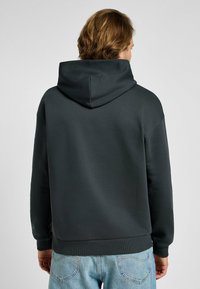 Sudadera gris oscuro hecha de tela suave, con una gran capucha, dobladillo y puños acanalados. Costuras visibles y diseño sin costuras en los hombros.