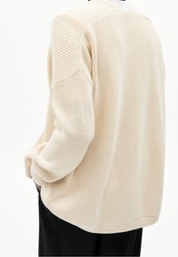 Béžový pletený svetr s volným střihem, s žebrovanou texturou, širokými rukávy a zaobleným lemem. Žádné viditelné logo ani vzory.