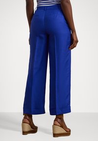 Pantalon bleu à jambes larges en tissu léger, avec un pli avant, des ourlets roulés et deux poches arrière. Assorti à des sandales compensées marron.