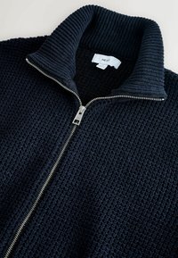 Marine zip-up trui met een gestructureerd breipatroon, geribde kraag en zilveren ritssluiting. Etiket zichtbaar binnenin de kraag.