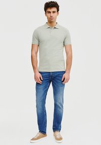 Jasnozielona koszulka polo, krótki rękaw, z kołnierzykiem i trzema guzikami. Połączona z niebieskimi dżinsami i jasnobeżowymi trampkami.