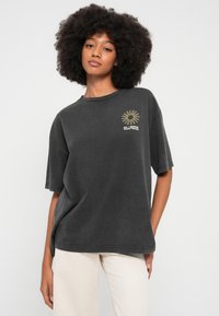 Bawełniany, luźny t-shirt w kolorze grafitowym, z krótkimi rękawami, z grafiką słońca i żółtym napisem "Billabong" po lewej stronie na wysokości klatki piersiowej.