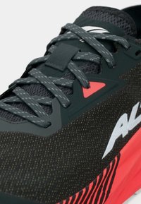 Sorte og grå atletik sko med teksturert mesh-overdel, røde detaljer og distinkt hvit logo, med grå snøringer og forsterkede snørehull.
