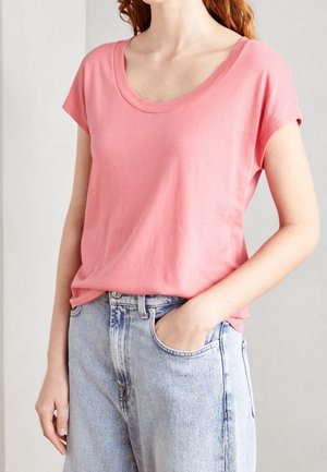 Femme portant un T-shirt rose à manches courtes, ample, légèrement rentré dans un jean en denim bleu clair taille haute, une main dans la poche.