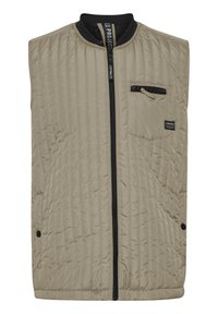 Gilet trapuntato beige con chiusura zip nera, colletto a costine e tasca sul petto sinistro. Presenta cuciture verticali e chiusure a scatto.