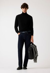 Maglione a collo alto nero, jeans blu scuro e scarpe nere. Tiene una borsa nera e una sciarpa grigia. Tessuto liscio, design aderente e trame sottili.