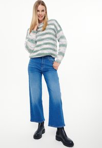 Sweter w pasiaki w kolorze zielonym i kremowym, zestawiony z niebieskimi spodniami typu wide-leg i czarnymi botkami za kostkę. Sweter ma luźny krój i ściągacze przy mankietach.