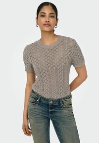 Lichtgrijze gebreide trui met korte mouwen, voorzien van een ruitpatroon, gecombineerd met blauwe denim jeans. Soepele textuur en een relaxte pasvorm.