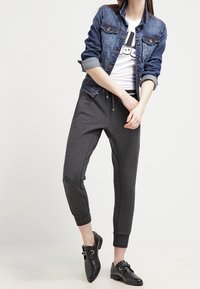 Jeansová bunda, modrá, s knoflíkovým zapínáním a ohrnutými manžetami; bílý tričko s grafikou; šedé tepláky; černé kotníkové boty s přezkami.