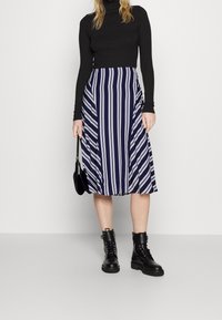 Černý rolák v kombinaci s tmavomodrou midi sukni s bílými pruhy. Černé šněrovací boty a malá černá kabelka dotvářejí vzhled.