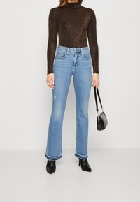 Haut marron côtelé à col roulé, jean évasé bleu clair avec des accents usés, talons noirs à bout pointu, petit sac à main noir.