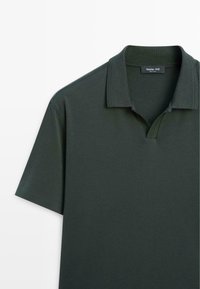 Polo vert foncé à manches courtes avec un col plié et une patte ouverte qui laisse apparaître l’étiquette Massimo Dutti à l’intérieur du col.