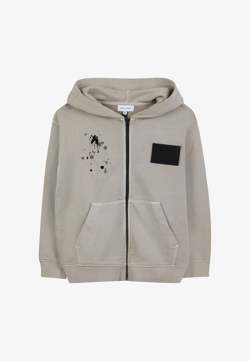 Haut à capuche zippé beige clair en mélange de coton, avec une poche avant, un patch en tissu noir et un design abstrait de éclaboussures de peinture noires et grises.