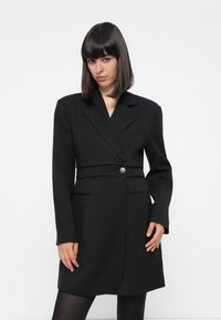 Svart skreddersydd blazer-kjole med lange ermer, krage, enkelt knappelukking og lommer. Glatt stoff med en strukturert passform.