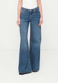 Blugi evazați de culoare albastru deschis, confecționați din denim, cu talie înaltă, două buzunare frontale și detalii subtile de cusături de-a lungul cusăturilor.