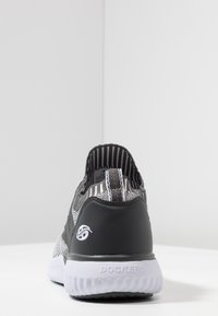 Zapatilla de rayas blanco y negro con parte superior de tela texturizada, talón negro sólido y suela de goma blanca. Presenta un logotipo en el talón.