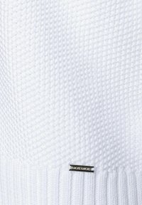 Weißer gestrickter Pullover mit strukturiertem Muster, mit geripptem Saum und einem kleinen metallischen Markenetikett auf der Vorderseite.