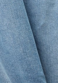 Țesătură din denim de un albastru deschis, cu o textură fină, cu rigle diagonale și variații subtile de decolorare, pliată pentru a evidenția adâncimea și calitatea materialului.