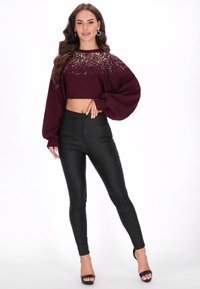 Bordeaux cropped trui met pailletten versieringen, gecombineerd met zwarte high-waisted lerenachtige leggings en zwarte sandalen met hak.