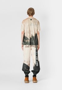 Conjunto de camiseta gráfica y pantalones con un diseño de paisaje, tonos beige con acentos oscuros, corte relajado y detalles de marca impresos.
