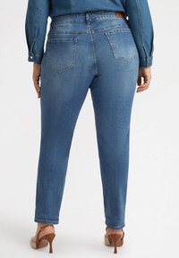 Vaqueros de mezclilla azul con diseño de pierna recta, que cuentan con dos bolsillos traseros y una cinturilla con una placa de cuero marrón. Textura suave.