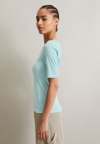  Lichtblauwe ribbel top met korte mouwen en ronde halslijn, passend ontwerp, gladde textuur, gecombineerd met gestreepte beige broek.