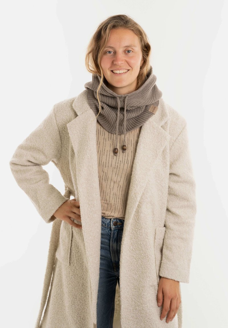 Beige oversized wollen mix jas, lichte trui met een textuurpatroon, grijze gebreide sjaal met trekkoord en houten accenten, blauwe jeans.