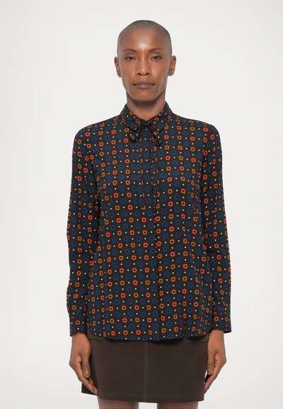 Blouse noire à motifs, avec des motifs floraux multicolores, col boutonné, manches longues et coupe décontractée, associée à une jupe marron.