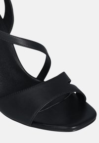 Sandal in pelle nera con tacco, caratterizzato da cinturini incrociati, design open toe e superficie liscia. Puntale quadrato con un'estetica minimalista.