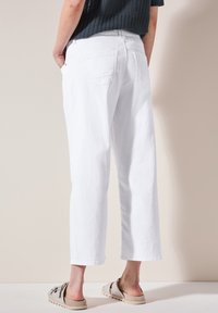 Pantalones de mezclilla blancos con un ajuste relajado, largo recortado y diseño de cinco bolsillos. Llevados con unos zapatos de lona de color claro.