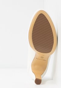 Podešev bílých dámských vysokých bot s béžovým a hnědým protiskluzovým gumovým gripem a malým blokovým podpatkem.