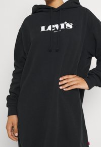 Robe sweat à capuche noire avec logo blanc "Levi's", cordons de serrage et poignets côtelés. Confectionnée dans un tissu doux avec une coupe décontractée.