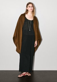 Brun poncho över en svart linne, matchat med en svart kjol och röda flip-flops. Silverhalsband med ett hänge och ringdetaljer synliga.