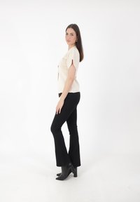 Top corto de color crema con cortes redondeados, combinado con jeans negros acampanados y botas negras de tacón, sobre un fondo blanco liso.