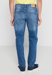 Jeans de denim azul con un corte ajustado, que presentan una etiqueta de cuero en la cinturilla, dos bolsillos traseros y un ligero desgaste.