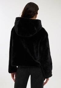 Czarna bluza z futerkiem o miękkiej teksturze, z obniżonymi ramionami i luźnym krojem. Posiada przestronną kieszeń i mankiety. Klasyczny design.