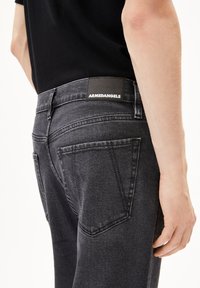 Slim-fit donkergrijze jeans van denim, met een zwart merklabel op de tailleband en gestructureerde achterzakken.