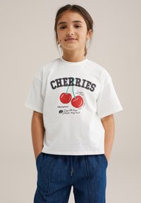 Balta medvilnės marškinėliai su "VYNUOGĖMIS" grafika, vaizduojančia dvi raudonas vyšnias ir linksmą tekstą. Trumpi rankovės, laisvas kirpimas, ripsuota apykaklė.