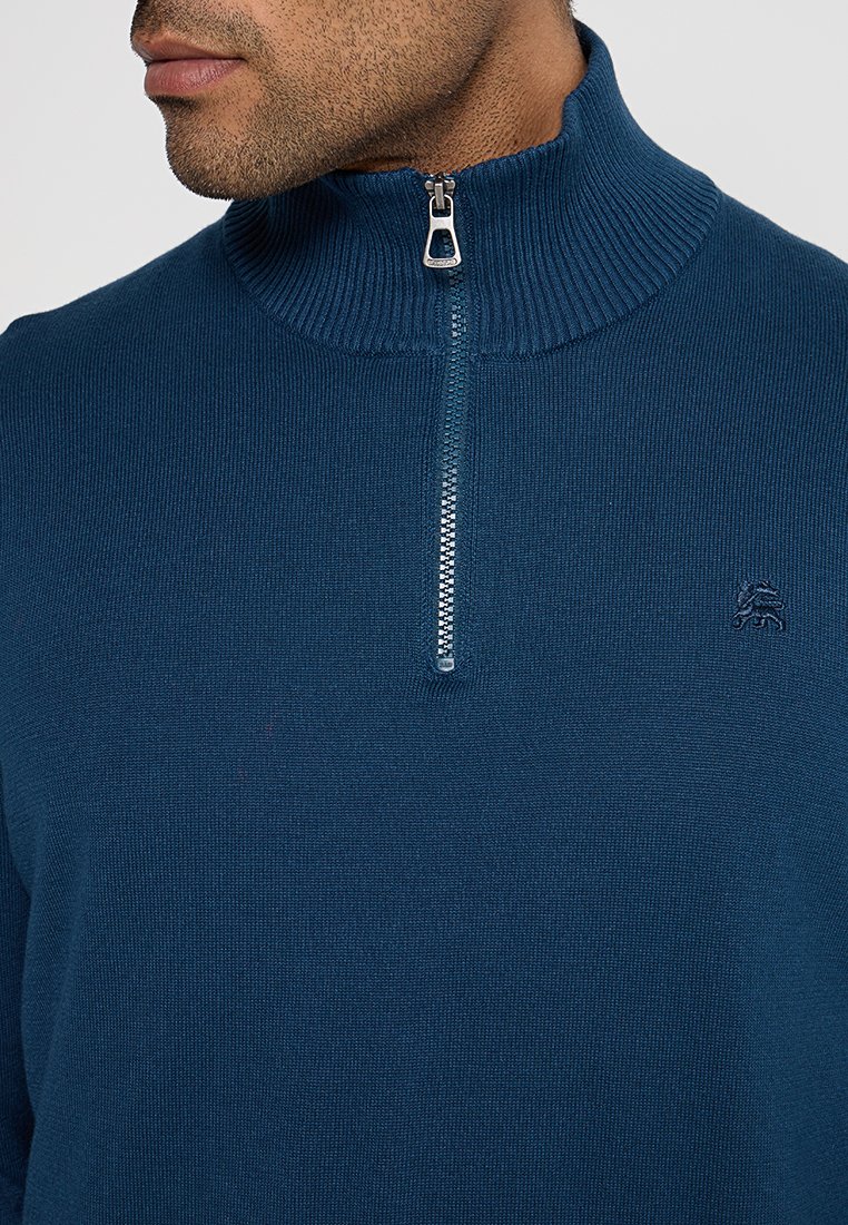 Granatowy sweter z wysokim prążkowanym kołnierzem i półzamkiem. Posiada subtelną fakturę oraz małe logo na lewej piersi.