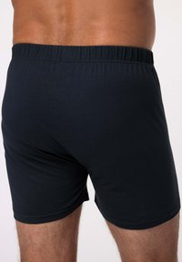 Siniy puuvillane bokseripüksid elastse vöökohtaga ja õmblusteta disainiga, rõhutades siledat tekstuuri ja tihedat istuvust.