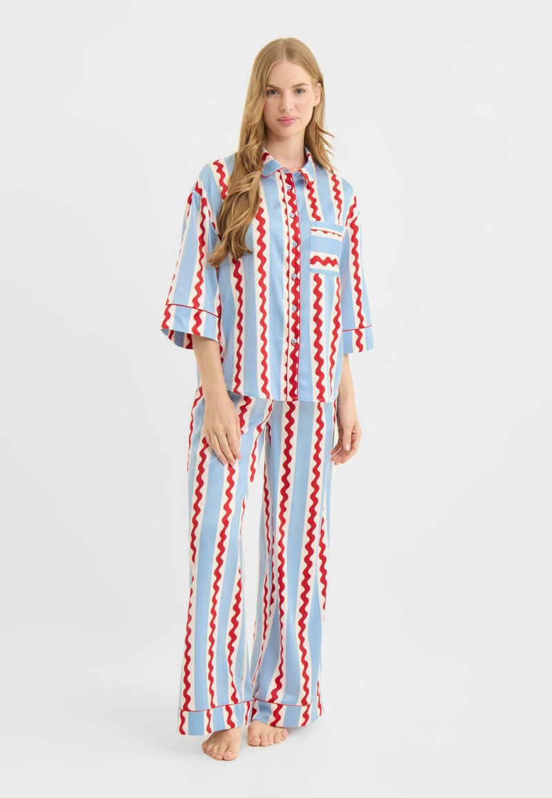 Blåt, rødt og hvidt stripet pyjamassæt med zigzag-mønstre. Inkluderer en skjorte med knapper og lomme samt løstsiddende bukser.