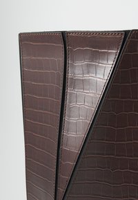 Hnedá umelá taška z krokodílej kože s elegantným geometrickým dizajnom, vybavená lesklým povrchom, výraznou textúrou a kontrastným prešitím.